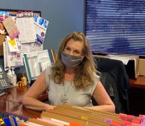 Marcie Whited at desk with Covid-19 Mask